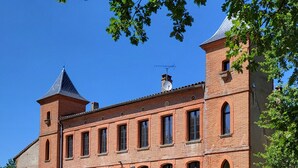 A large brick building with a central courtyard, featuring outdoor seating and a clock tower. - Castle 15mn Toulouse Pyrénées' view and pool (Clermont-le-Fort)