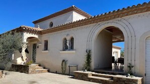 Un edificio con techo de tejas, entrada arqueada y una escalera de piedra que lleva a un porche cubierto.