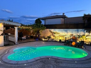 Une piscine à bordures courbes, entourée d’une zone pavée et agrémentée d’un mur décoratif orné de plantes et d’éclairages.