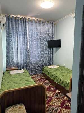 A small, well-lit room with two single beds, a television mounted on the wall, and a patterned carpet. - Mamnun Hotel (Bukhara)