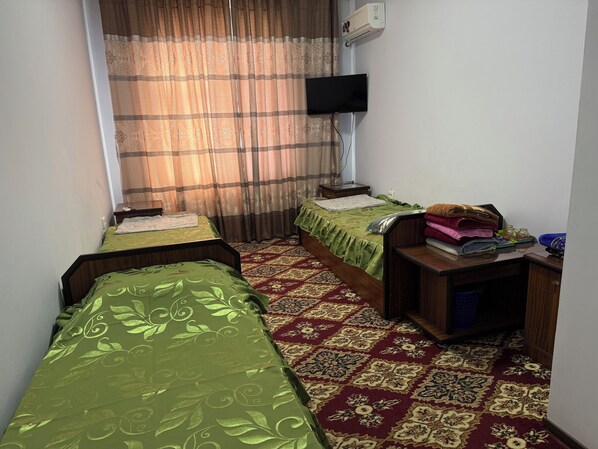 A room with two single beds, a flat-screen TV, a heater, and a small table with towels and toiletries.