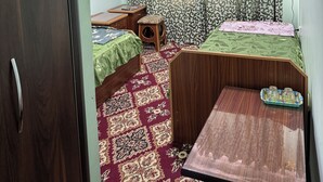 Een slaapkamer met twee enkele bedden, een klein tafeltje, een aan de muur bevestigde televisie en kamerbreed gordijn.