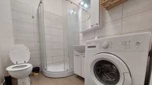 A modern bathroom with a toilet, a glass-enclosed shower, and a front-loading washing machine. - Magheru Studio Central (Bucharest)