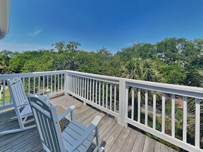 A wooden deck with white railings, two white Adirondack chairs, and a view of lush greenery and trees.