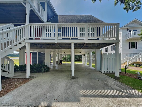 A covered outdoor area with a staircase leading to a second floor, surrounded by white railings and columns.