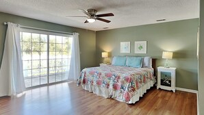 Un dormitorio amplio con un gran ventanal, un ventilador de techo y dos lámparas de noche.