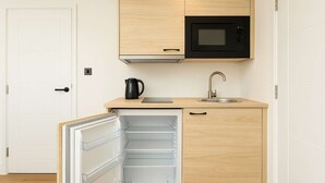 A compact kitchen with a microwave, sink, and a refrigerator with open shelves.