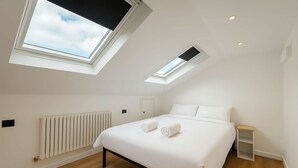 A modern bedroom with a skylight, a bed, a bedside table, and a radiator.