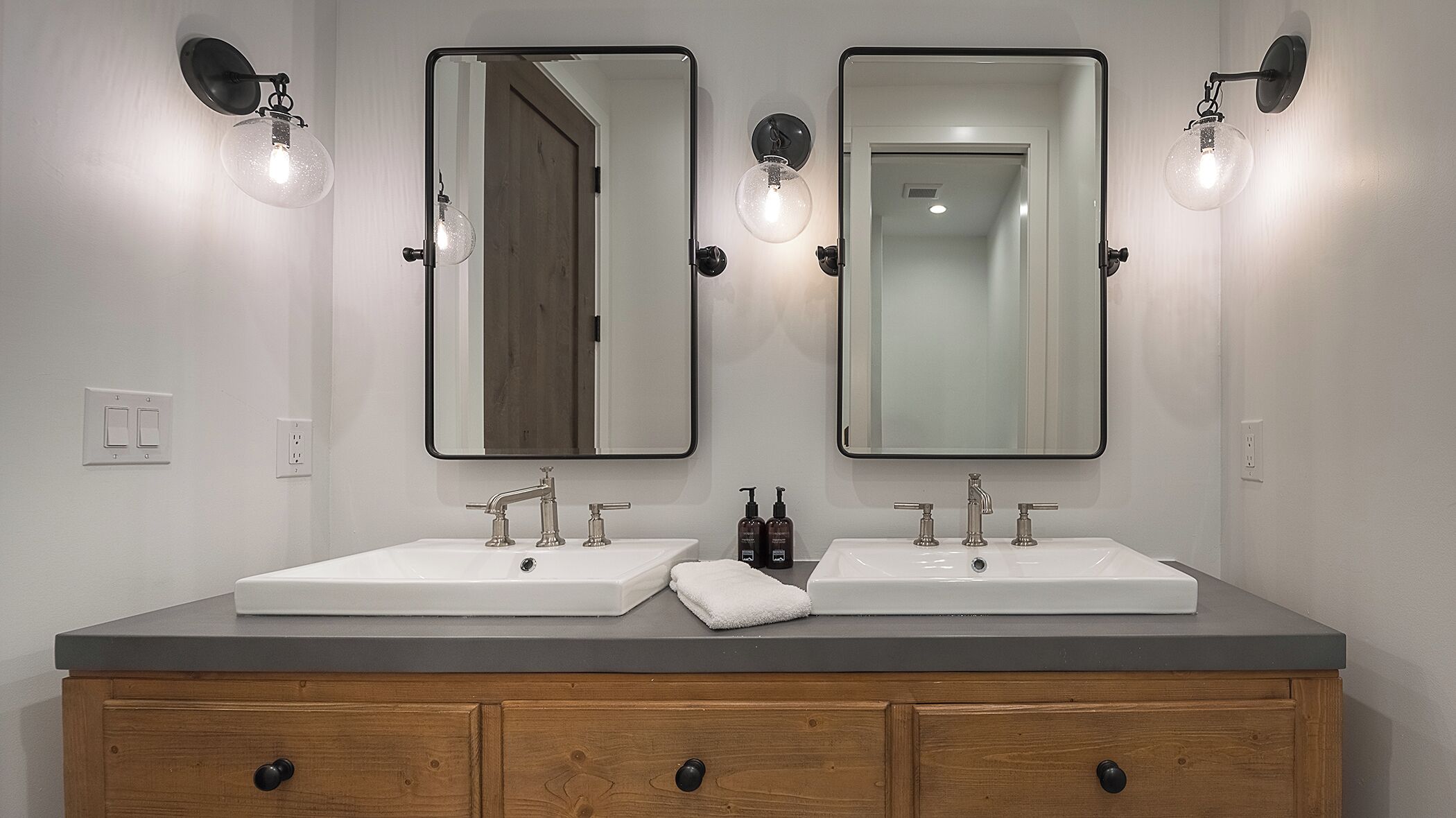 Un baño con dos lavamanos, un mueble de tocador de madera y espejos montados en la pared.
