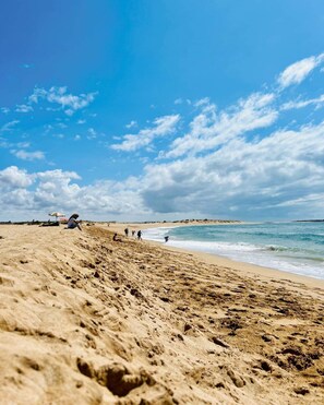 Une plage où l’on voit des empreintes de pas menant à l’eau, quelques personnes et un ciel dégagé.