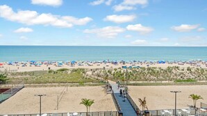 A beach with a walkway leading to the water, umbrellas, and beachgoers. - Family Friendly condo w/ Pools by Seaside Vacations & Sales (Ocean City)