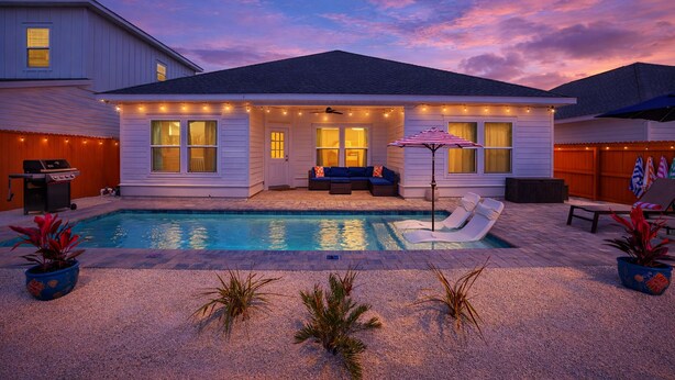 A house with a swimming pool, outdoor seating, and string lights.