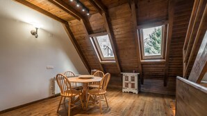 Une pièce mansardée accueillante, avec une table et des chaises en bois, un petit meuble et une fenêtre donnant sur les arbres.