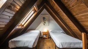 Une petite chambre mansardée avec deux lits simples, une table de chevet avec une lampe et un plafond en bois.