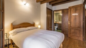 Une chambre avec un lit en bois, une table de chevet et un plafond en bois. Une porte donne accès à une salle de bain.
