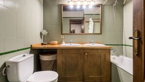 Une salle de bain avec deux lavabos, des toilettes, un miroir, une douche et un meuble de rangement.