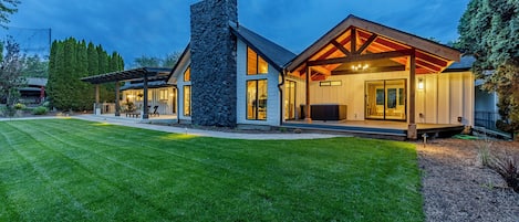Une maison moderne avec une cheminée en pierre, de grandes fenêtres et une véranda couverte.