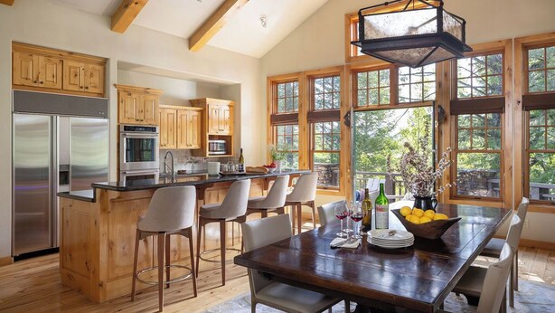 A spacious kitchen with wooden cabinets, a central island with bar stools, a large dining table, and a hanging light fixture.