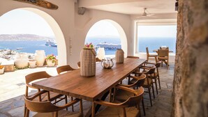 A wooden table with chairs, potted plants, and a view of the sea. - Eagles Nest Mykonos Adults Only (Tourlos)