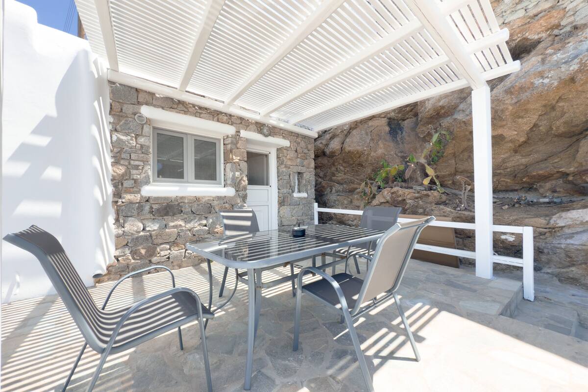 Une terrasse extérieure avec un mur en pierre, une porte blanche et une table entourée de chaises.