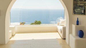 A room with a large arched window overlooking the sea, a white sofa, and a small table with a blue vase. - Eagles Nest Mykonos Adults Only (Tourlos)
