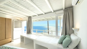 A bedroom with a large window, a bed, a desk, and a view of the sea. - Eagles Nest Mykonos Adults Only (Tourlos)