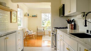 A kitchen with white cabinets, a wooden chair, and a TV mounted above the stove. - The Captain's Cottage on Shoreline Drive (Santa Barbara)