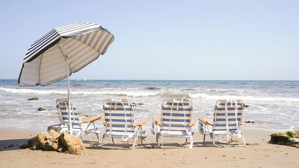 A beach with three striped lounge chairs under a striped beach umbrella, facing the ocean. - The Captain's Cottage on Shoreline Drive (Santa Barbara)
