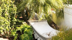 A garden with a variety of tropical plants, a white bench, and a stone pathway. - The Captain's Cottage on Shoreline Drive (Santa Barbara)