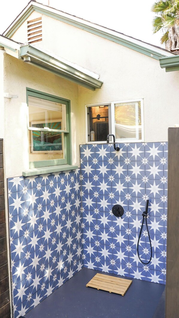 A small, enclosed shower area with blue star-patterned tiles, a wooden bench, and a window with a view of the interior.