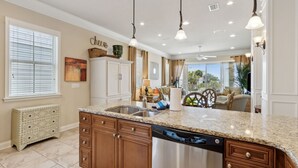 A kitchen with granite countertops, wooden cabinets, and a dishwasher. There is a window with blinds, a radiator, and a ceiling fan.