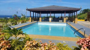 Une piscine dotée d’un espace détente couvert, entourée de plantes tropicales et offrant une vue sur l’océan.