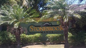 Une enseigne pour Stonebrook Manor, avec un décor tropical en arrière-plan.