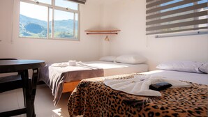 A bedroom with two beds, a table, and a window with a view of mountains. - Hotel Plaza Centro Cocorná (Cocorná)