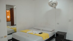 A single bed with a yellow blanket and white pillows, a bedside table with a remote control, and a wall-mounted fan. - Hotel Plaza Centro Cocorná (Cocorná)