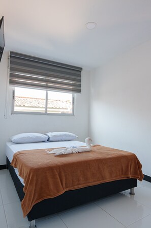Une chambre à coucher avec un lit, des oreillers blancs, une couverture marron et une serviette en forme de cygne.
