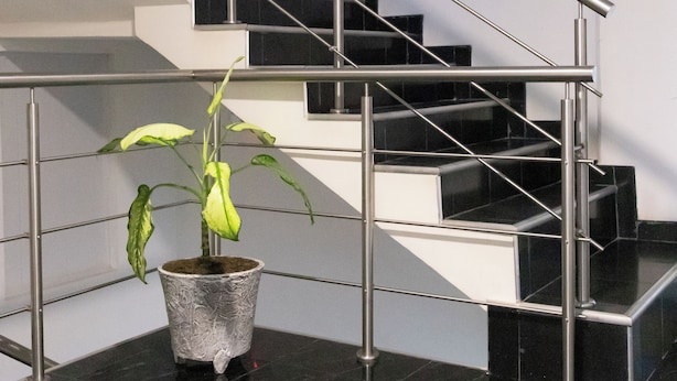A modern staircase with a metal railing, a potted plant, and black tiled flooring. - Hotel Plaza Centro Cocorná (Cocorná)