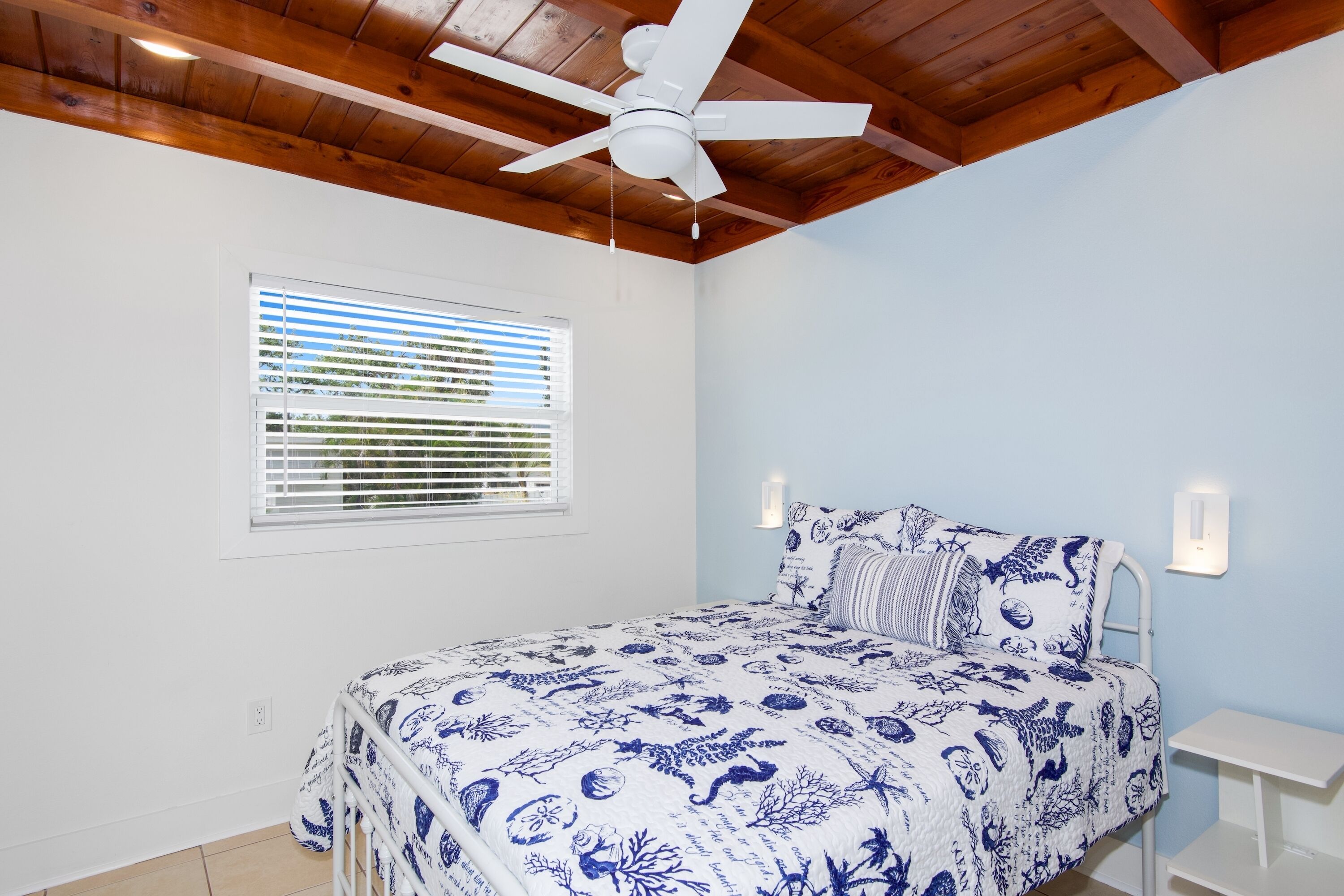 Une chambre à coucher avec un lit, un ventilateur de plafond, une fenêtre avec des stores et une table de chevet.
