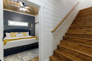 Une chambre à coucher avec un lit, un ventilateur de plafond, un escalier en bois et un tableau encadré au mur.