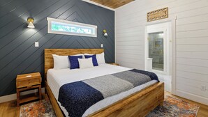 A bedroom with a wooden bed, a nightstand, a window with a view, and a door with a glass panel. - NEW Listing! Elevated forest views at Pines Peak! (Broken Bow)
