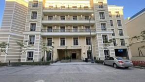 Un hôtel à plusieurs étages, doté d’une entrée principale, d’un espace de stationnement et d’une voiture garée devant.