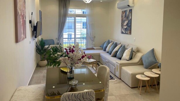 Un salon moderne comprenant un canapé, une table à manger avec des chaises, une table basse ornée d’un vase de fleurs et une grande fenêtre avec des rideaux.