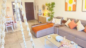 Un salon moderne comprenant un canapé, un pouf, une table basse et un coin repas avec des chaises et une table.