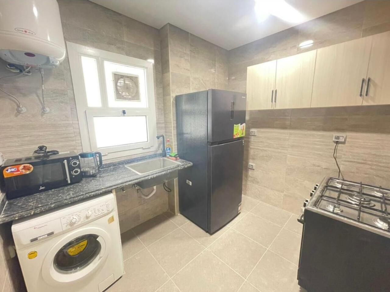 A compact kitchen with a washing machine, a refrigerator, a stove, and a window with blinds.
