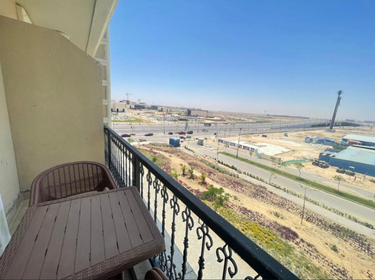 Ein Balkon mit Tisch und Stühlen, mit Blick auf eine Baustelle mit Gebäuden und Straßen.