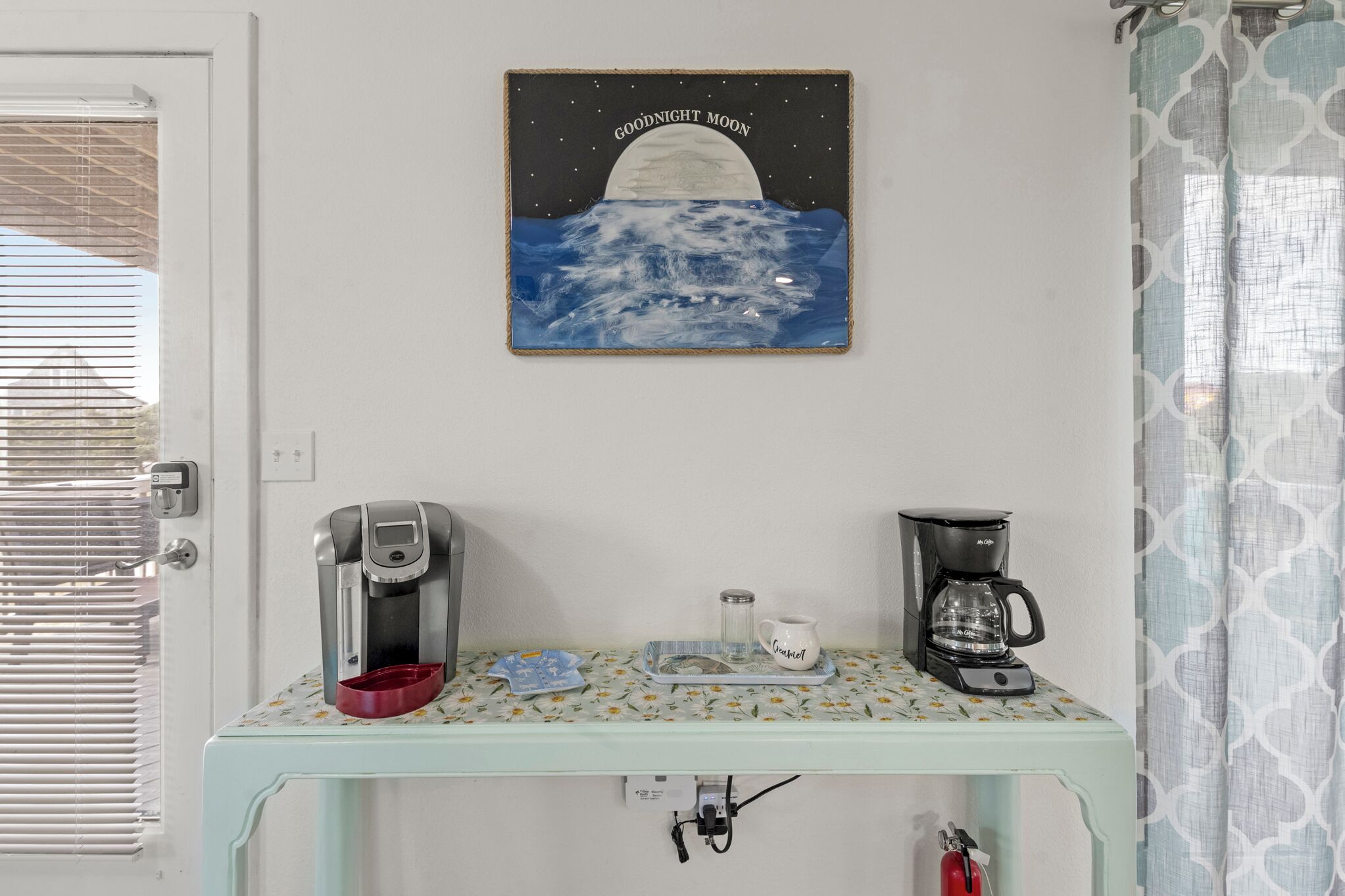 A kitchenette with a coffee maker, a mug, and a glass pitcher on a patterned tray.