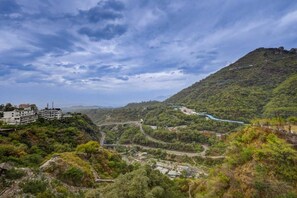 A mountainous landscape with a winding road, buildings, and a river. - Hotel Vinayak -Banganga Road Katra  (Reasi)