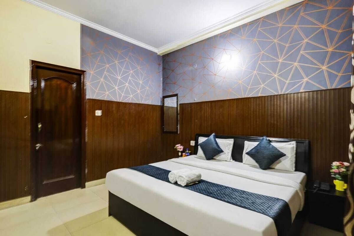 A hotel room with a large bed, wooden paneling, and a geometric patterned wall.