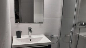A bathroom with a white sink, a mirror, a black cabinet, and a glass shower enclosure. - Quiet T1 in St Marc sur Mer, 5 min walk to the beach, terrace and large bed! (Saint-Nazaire)