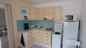 A compact kitchen with wooden cabinets, a microwave, a refrigerator, and a coffee maker. - Quiet T1 in St Marc sur Mer, 5 min walk to the beach, terrace and large bed! (Saint-Nazaire)
